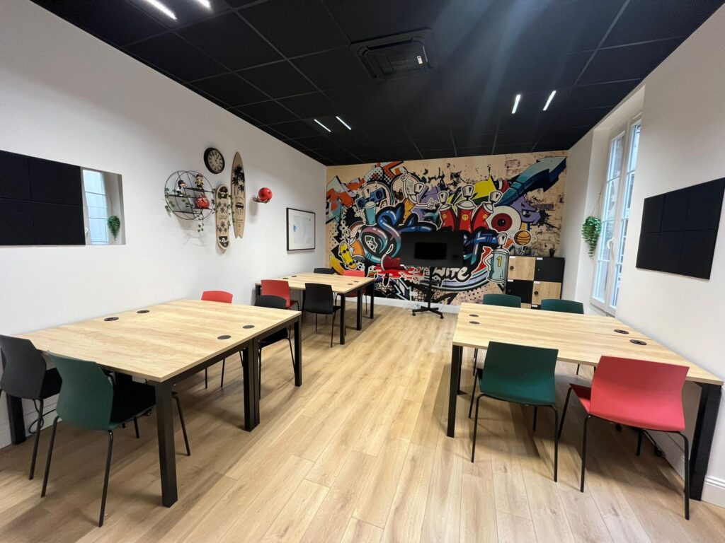 Salle de réunion moderne avec tables claires, chaises colorées (rouge, vert, noir), plafond noir et mur d'accent graffiti vibrant.